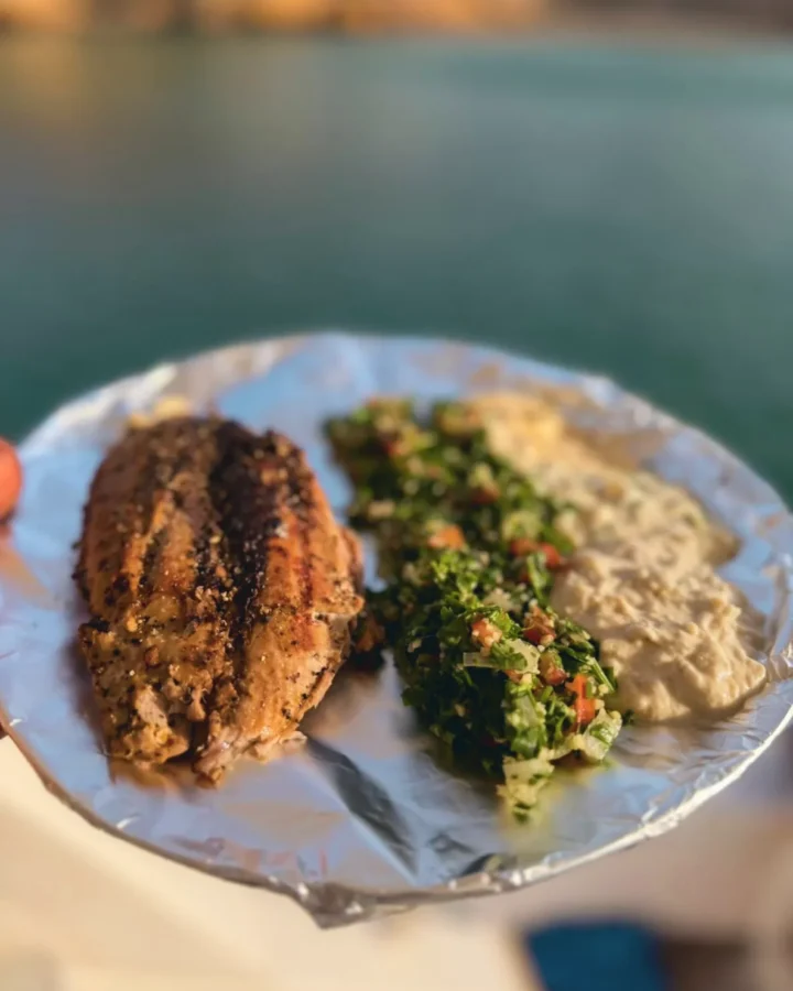 Grilled fish with tabbouleh and hummus, served by the water
