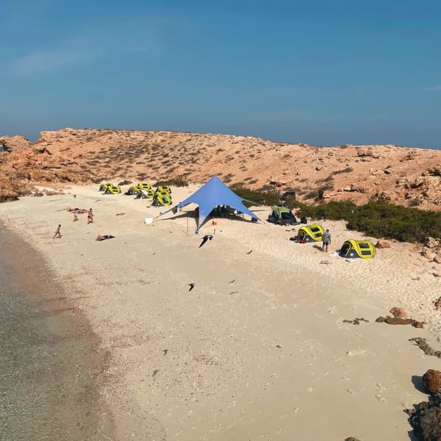 Tents and a shade canopy on a white-sand island beach