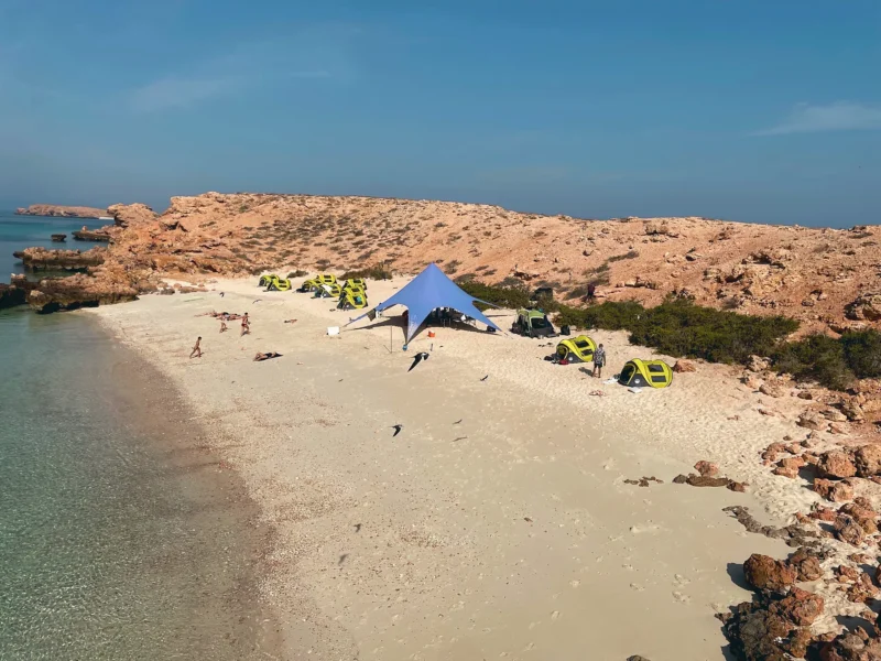 Tents and a shade canopy on a white-sand island beach