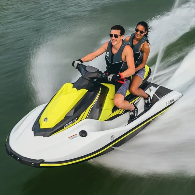 Two riders on a yellow and white jet ski, carving a wide wake
