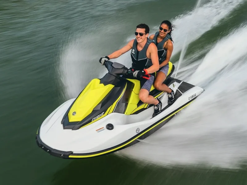 Two riders on a yellow and white jet ski, carving a wide wake
