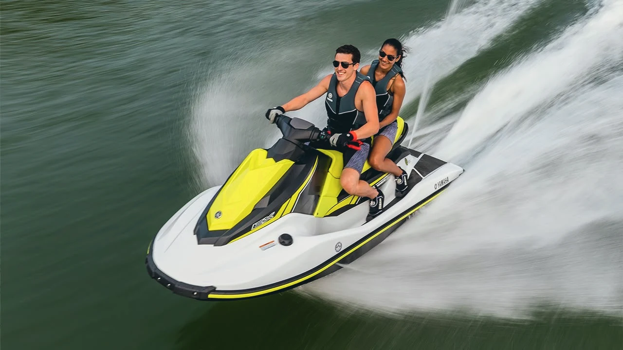 Two riders on a yellow and white jet ski, carving a wide wake
